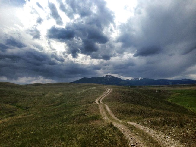 two track trail follows a ridge into the distance, mountain behind with dark storm clouds  in sky