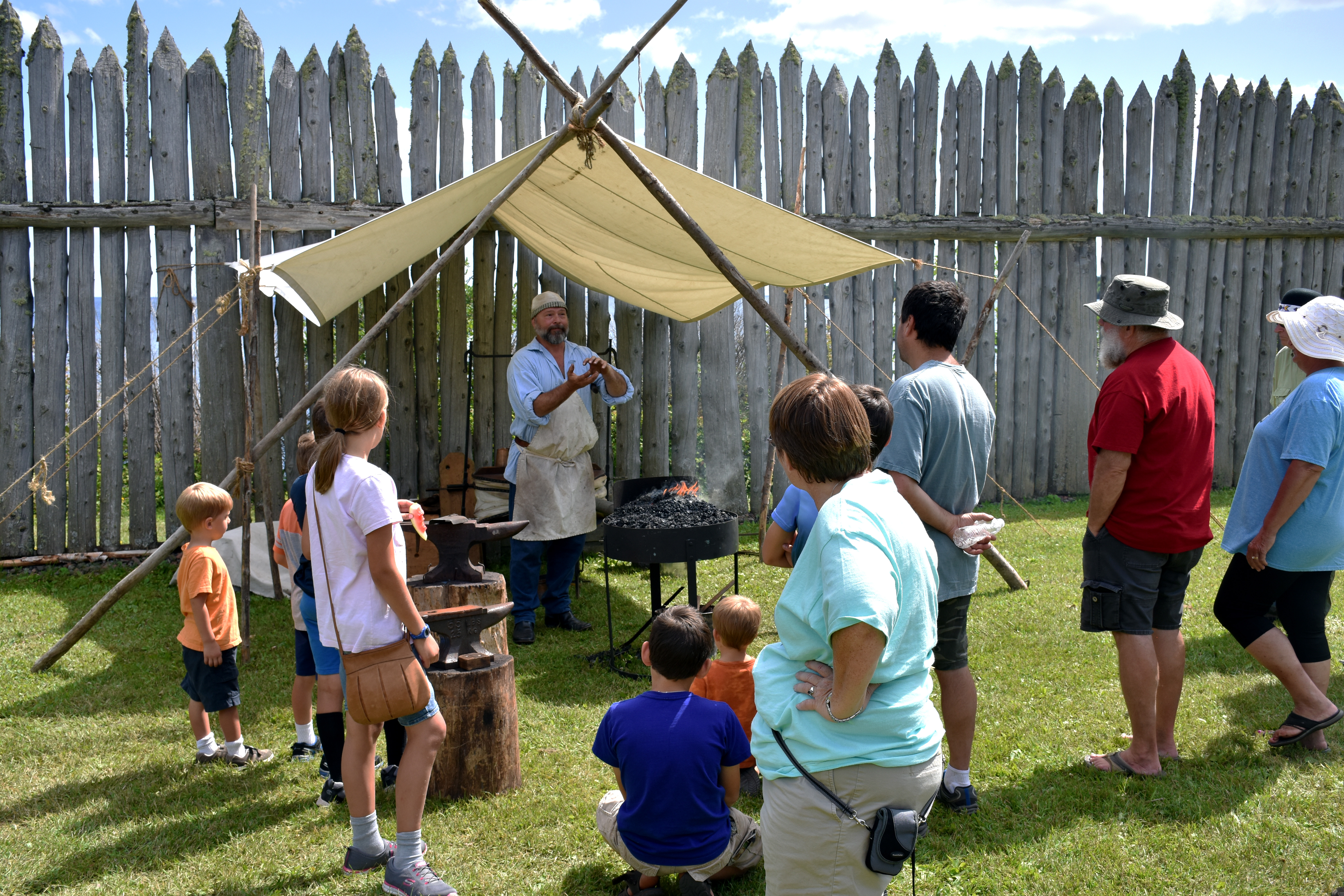 A costumed blacksmith with glowing coals with an audience.