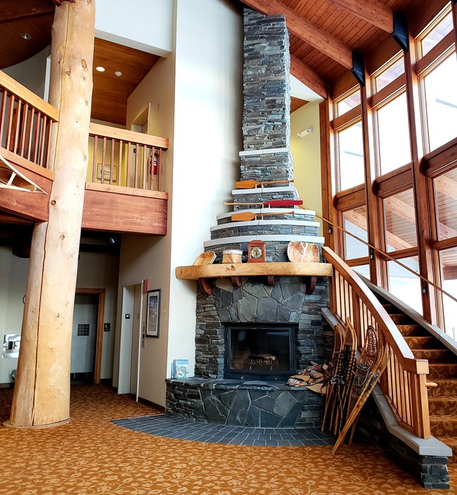 A tall fireplace made of stone in a carpeted lobby, next to a winding staircase.