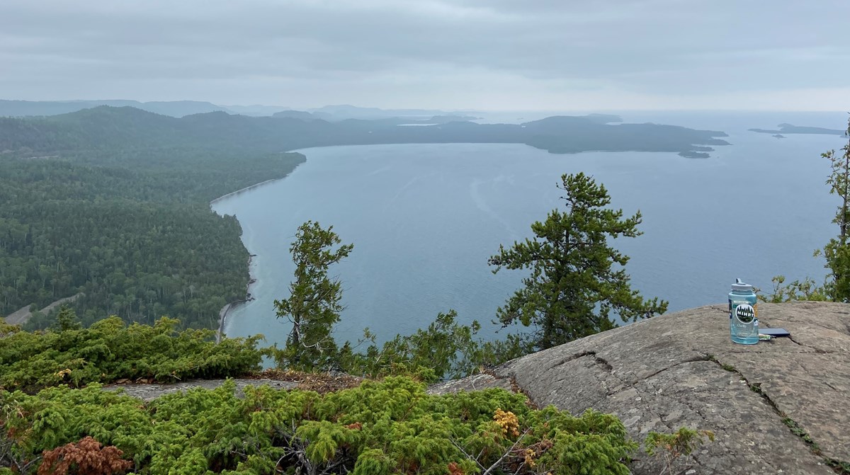 View of a peninsula and islands from the top of a mountain with a rock in the foreground and a forest below.