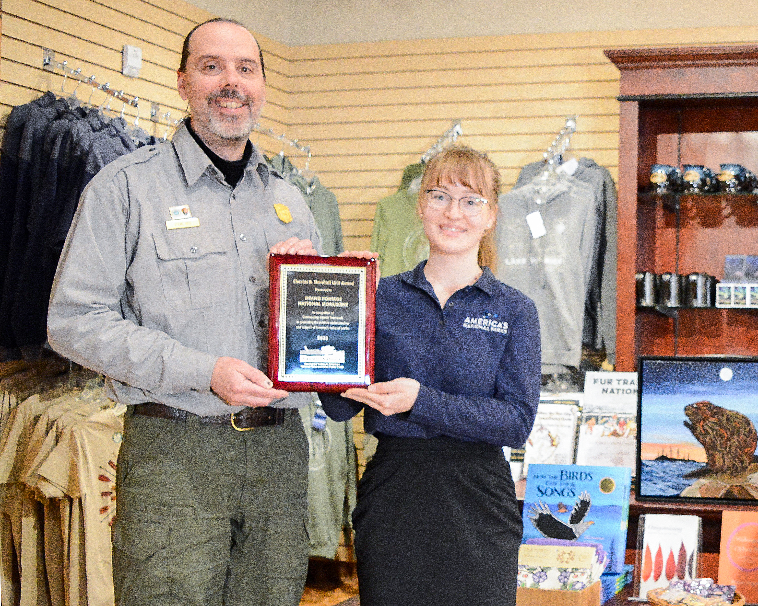 A woman in a copperating association uniform and a man in NPS uniform smile at the camera while holding an award together.