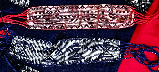 A pair of beaded garters - one red and white, one blue and white with animal motifs.