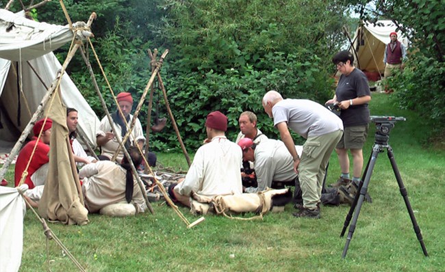 Film producers work with actors in an encampment scene.