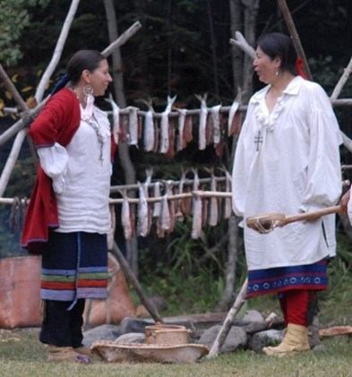 Women dressed in historic clothing in front of fish drying over a fire.