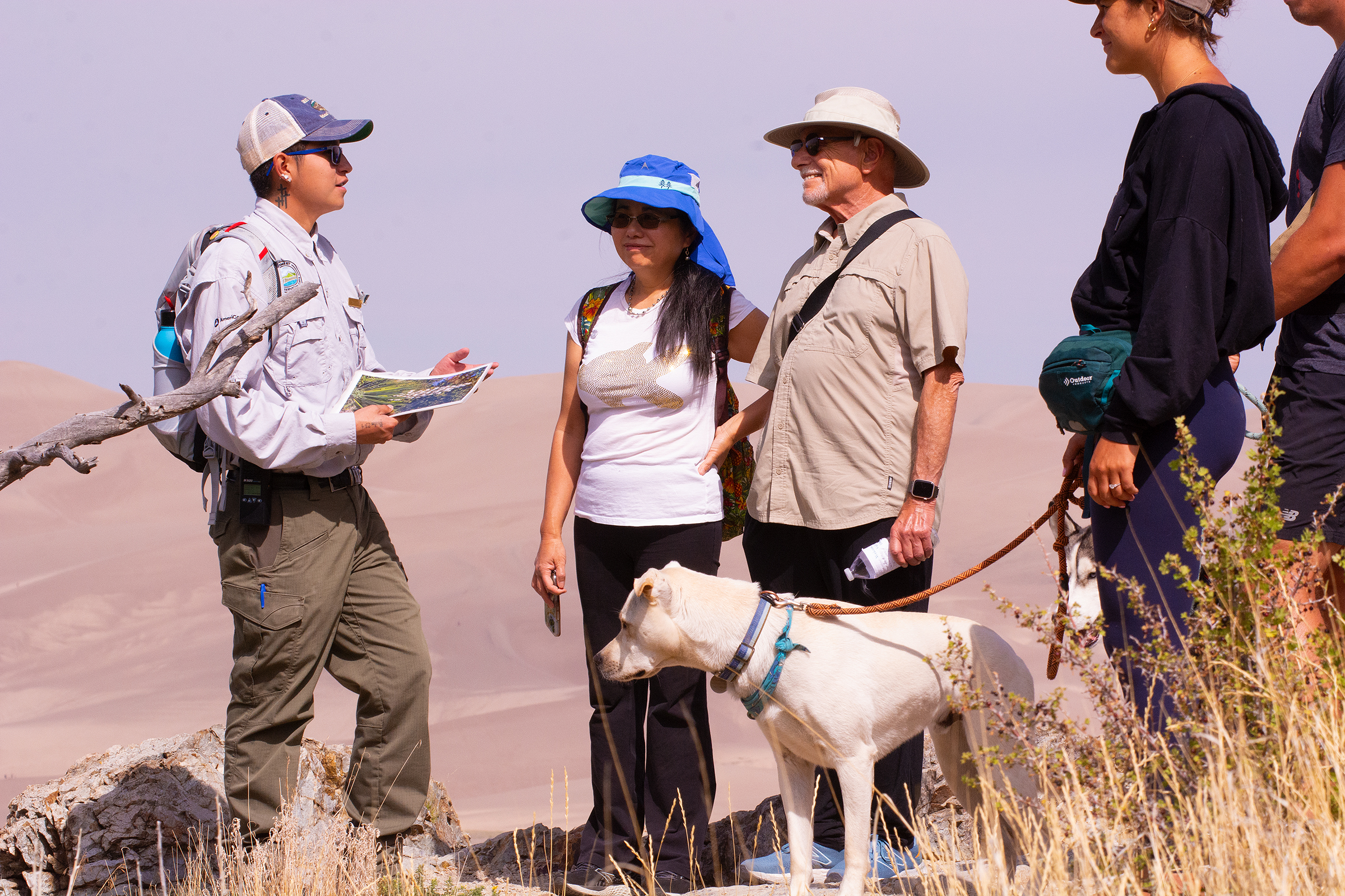An intern in uniform talks with visitors in front of the dunes.