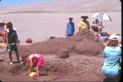 A family makes a sand sculpture of Jabba the Hutt along the Medano Creek bed at the base on the dunes in 2003.
