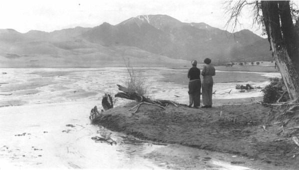 Historical black and white photo of Julia and Mary Herard beside a shallow stream flowing around the dunes