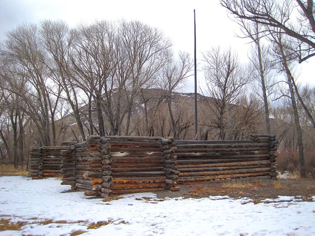 A log fort in the snow beside barren winter trees. A flagpole rises over the fort.