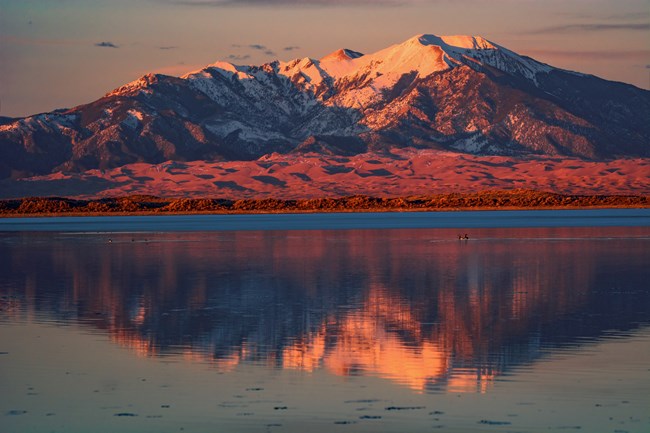 A lake at sunset with dunes and a snow-covered mountain beyond