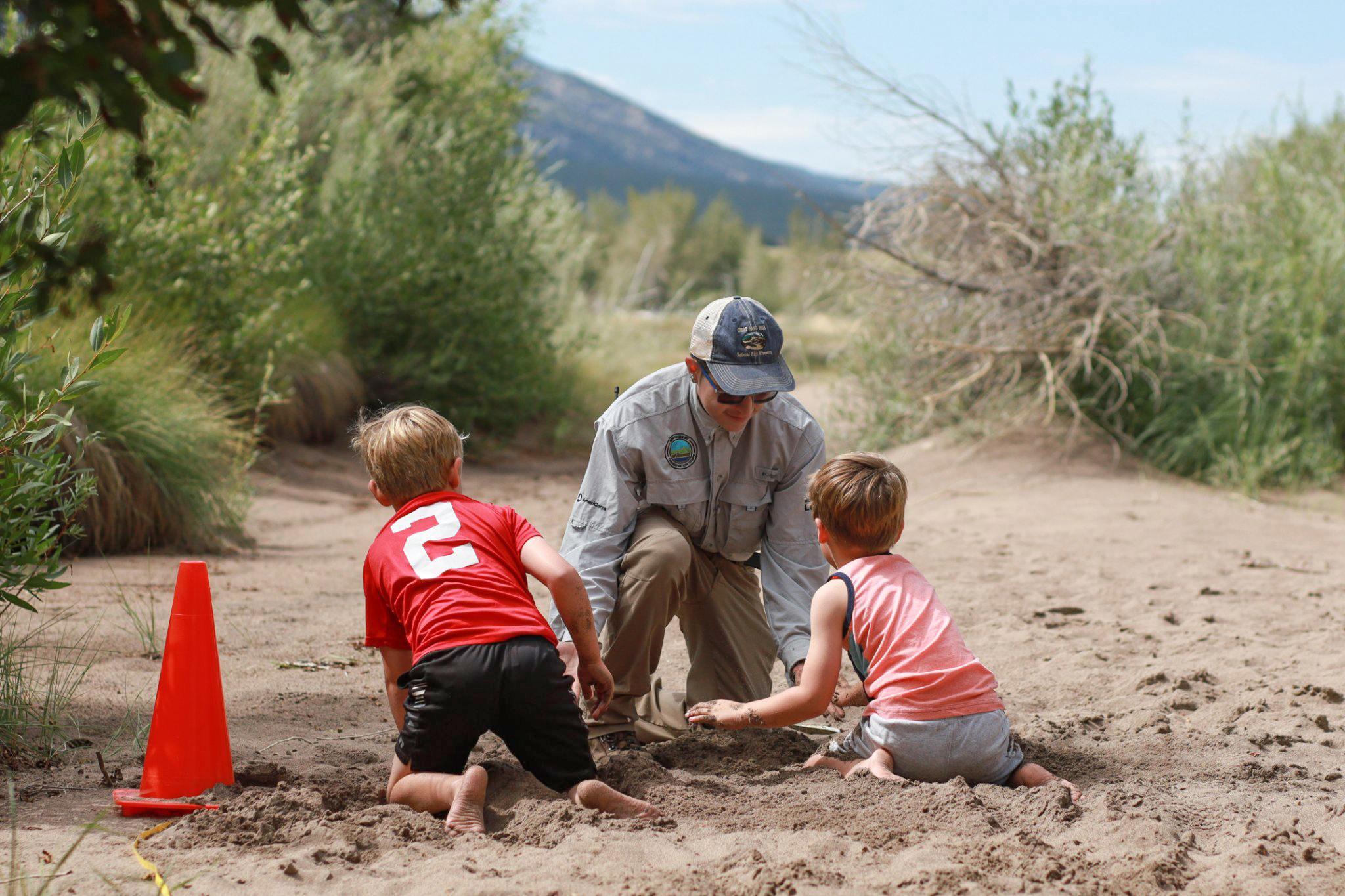 Intern Jaiden Garcia with Children at Junior Ranger Day An intern in uniform helps two children in the sand during Junior Ranger Day 2022