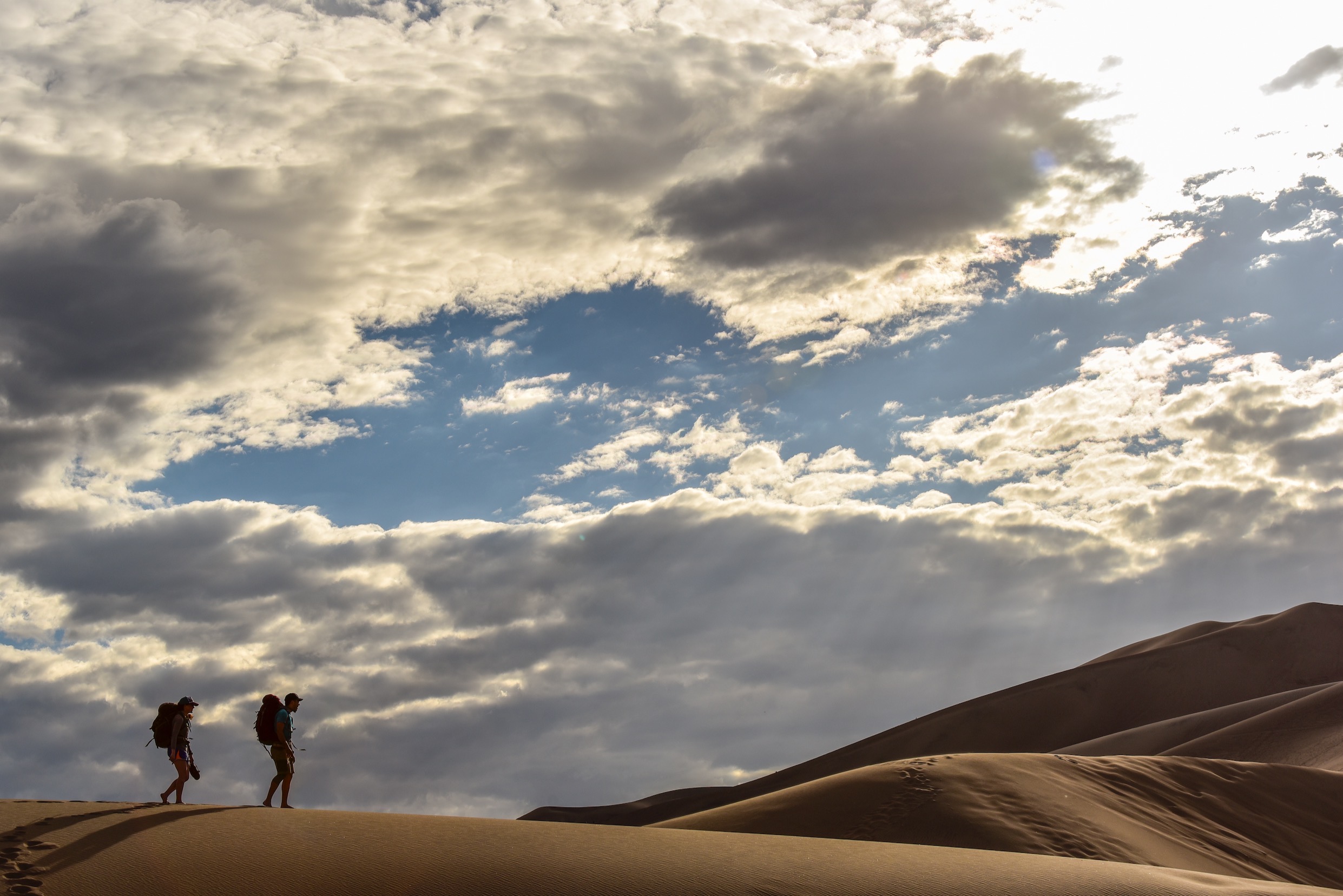 Two backpackers climb the high ridge line of dunes through the Day Use Area.