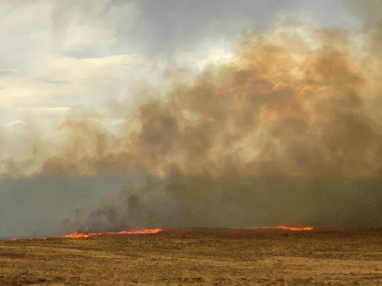 A line of wildfire burns through grasslands southwest of the dunes