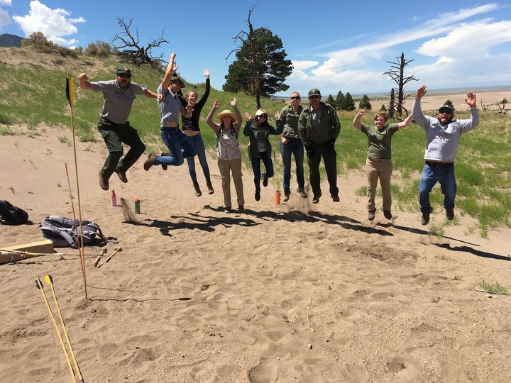 Park rangers and interns jump in a landscape of trees and dunes