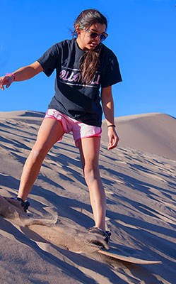 Teen girl standing on a sandboard at the top of a dune