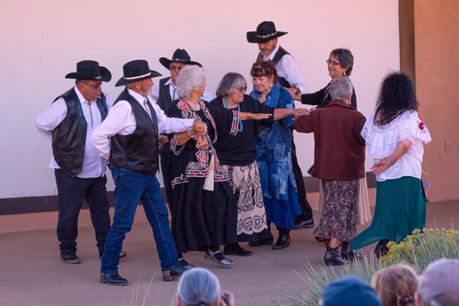 Spanish dancers promenade in a circle with men in black and white and women in dresses