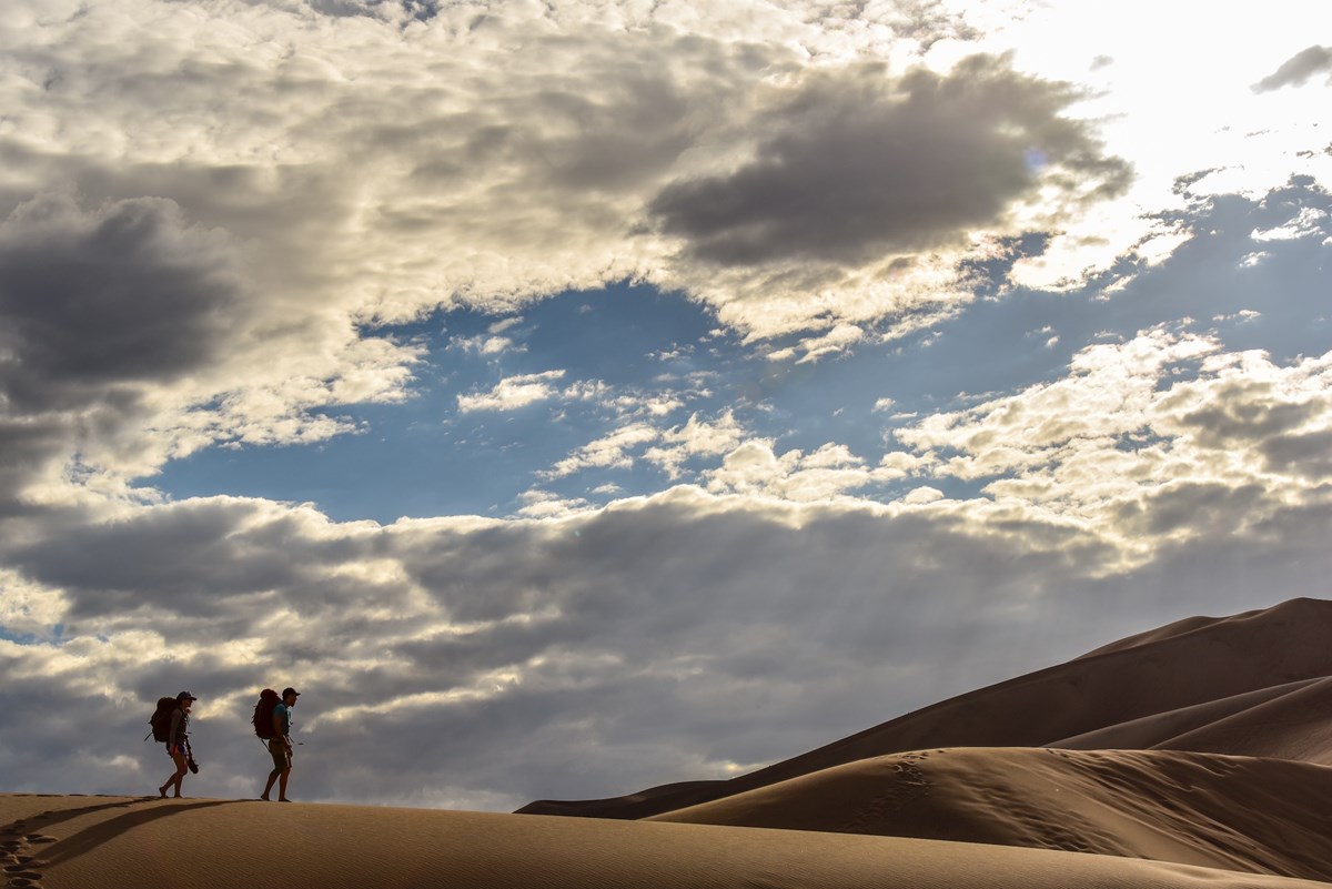 Backpackers are seen climbing the dunes near sunset to reach the Dunes Backcountry- located west of the highest ridgeline.