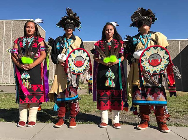 Four Navajo dancers stand in colorful regalia