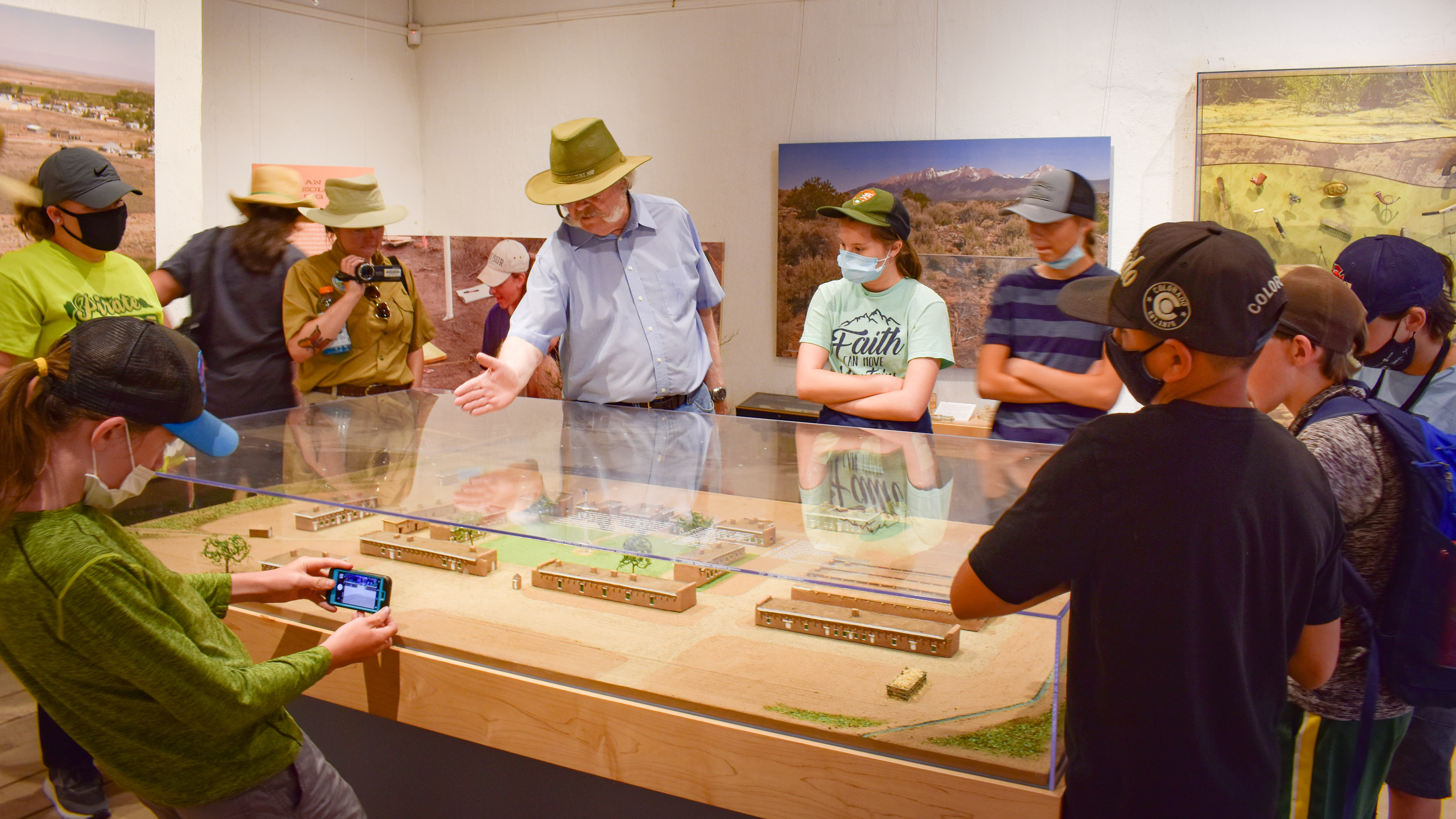 Family Archeology Days Fort Garland A group of children standing around a glass display case of artifacts with a museum docent