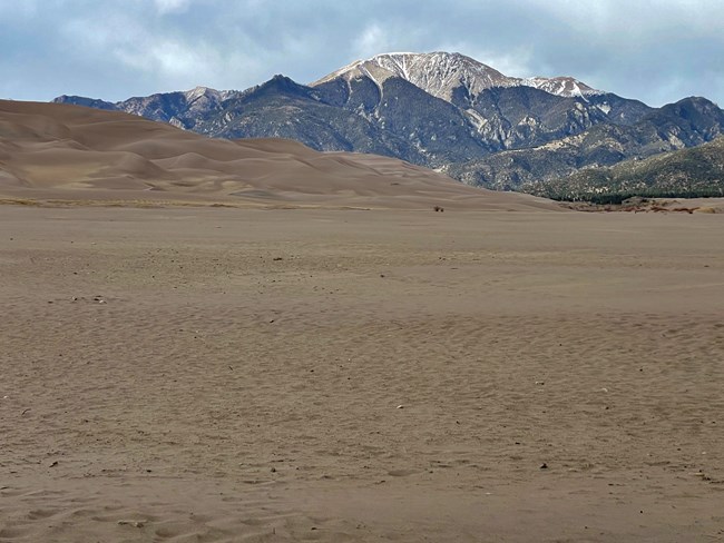 A dry sandy creek bed with dunes and a mountain with little snow