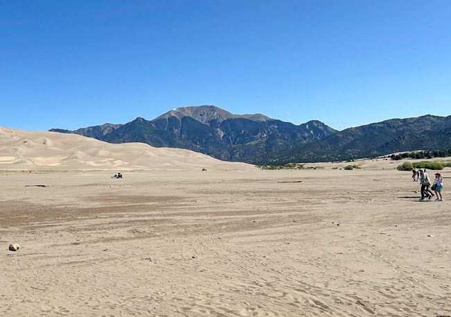 A flat dry expanse of sand with dunes and mountains in the background