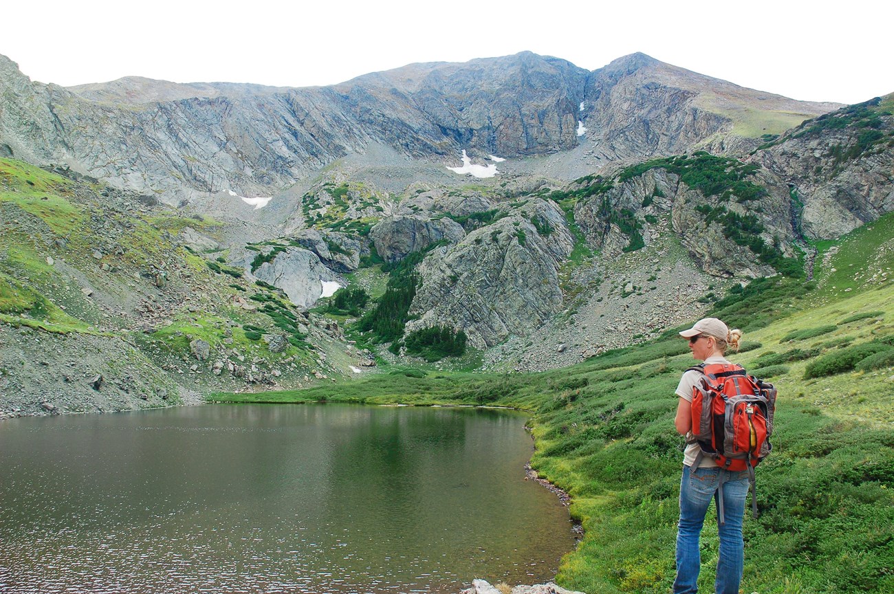 A hiker stands at the edge of Medano Lake- an alpine tundra lake in Great Sand Dunes National Preserve