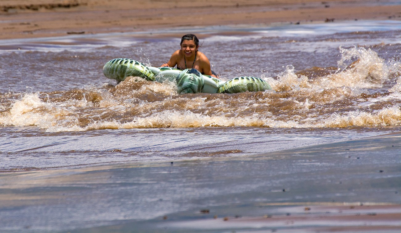 A girl rides on a wave in Medano Creek using a floatation device
