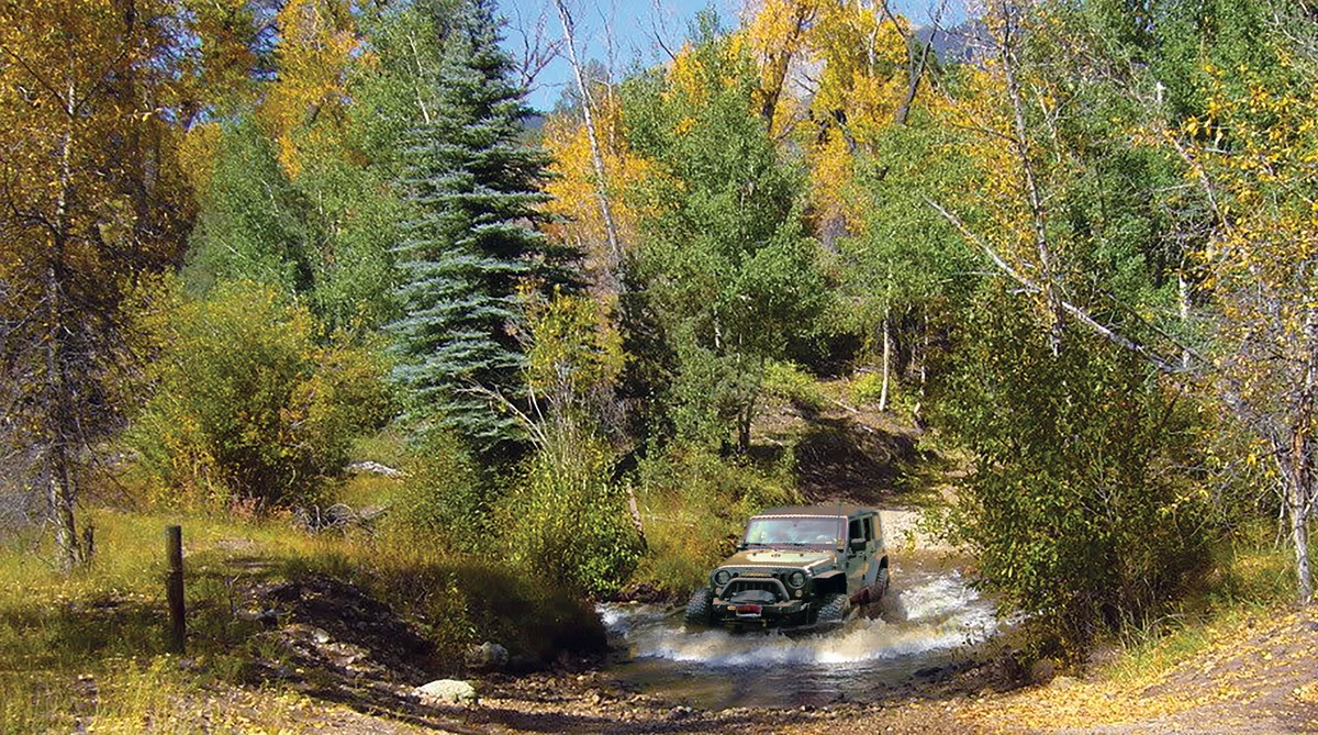 A Jeep crossing a mountain stream amid trees with fall colors