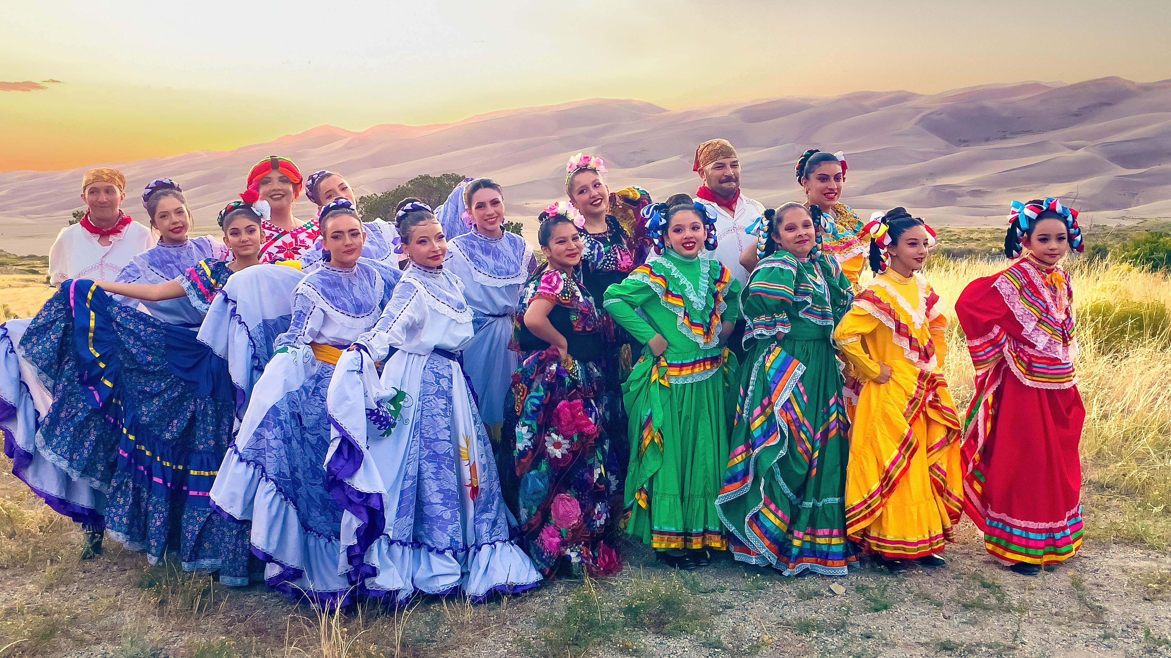 A large group of Hispanic dancers in Mexican dress stand in front of the dunes