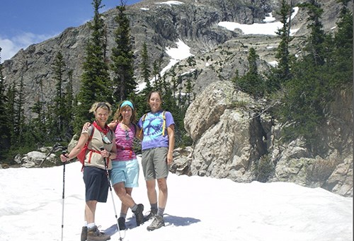 Three women standing in an in alpine area with snow, trees, and tundra