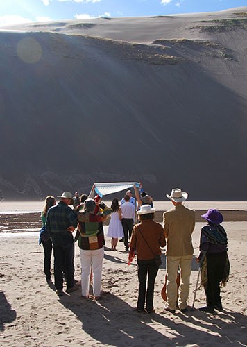 Wedding party gathered in front of a dune and Medano Creek