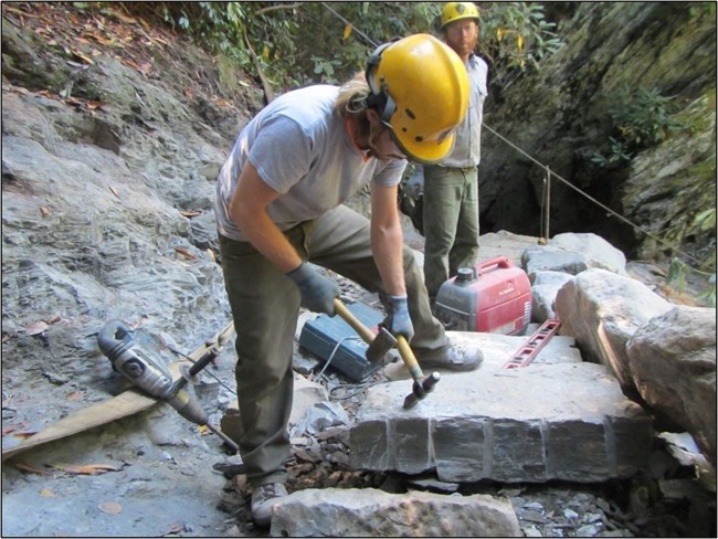 Volunteer chiseling rock on a trail in the backcountry.