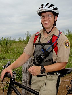 A bike patrol volunteer standing beside a field in Cades Cove