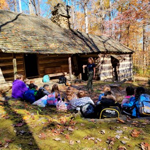 Students and ranger in front of cabin in forest.