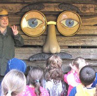 Ranger standing next to “Barney” the barn, a barn with the face of an old man. The ranger holds up 3 fingers while teaching the students.