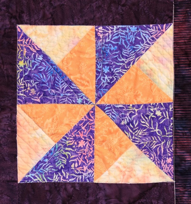 A Double Pinwheel Block that has a swiral like pattern in purple and yellow.