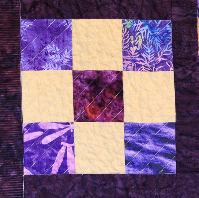 A nine patch purple and yellow quilt block.