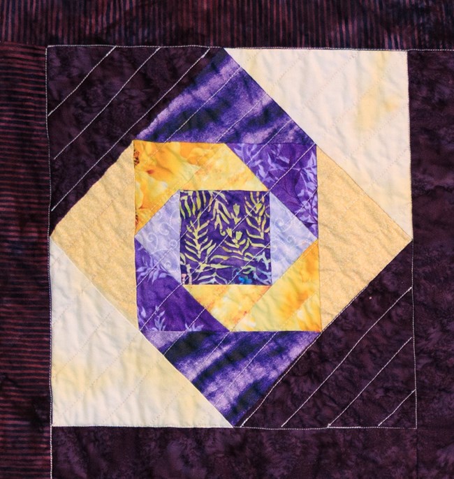 A quilt block with squares and diamonds that is purple and yellow.