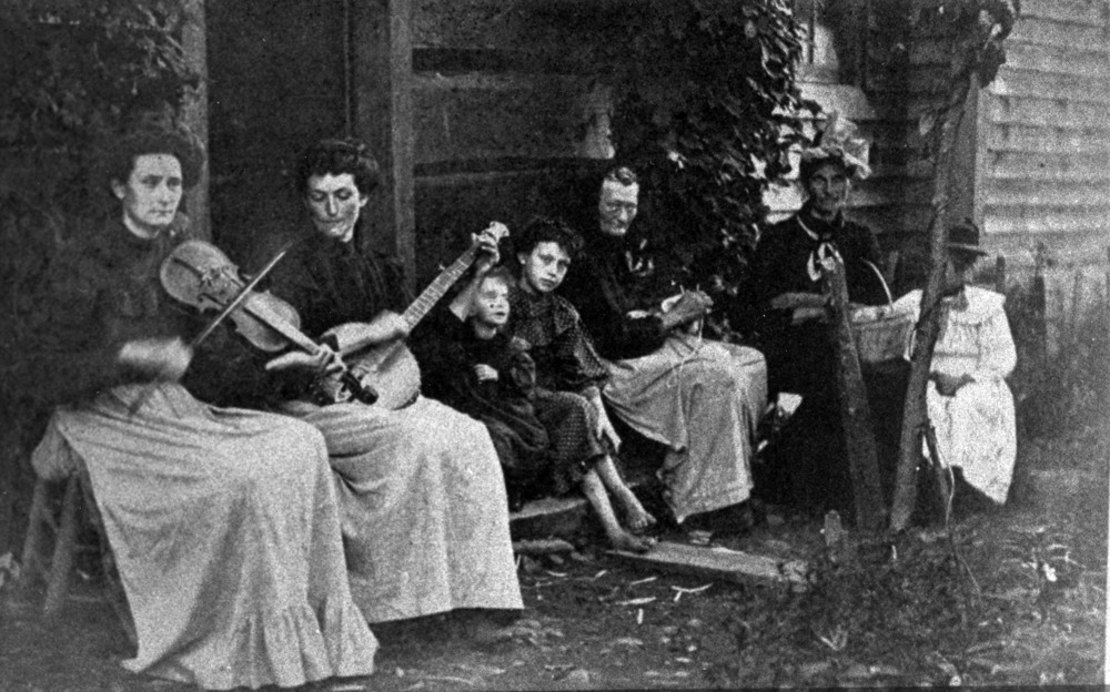 Women and children sitting on a porch with instruments making music
