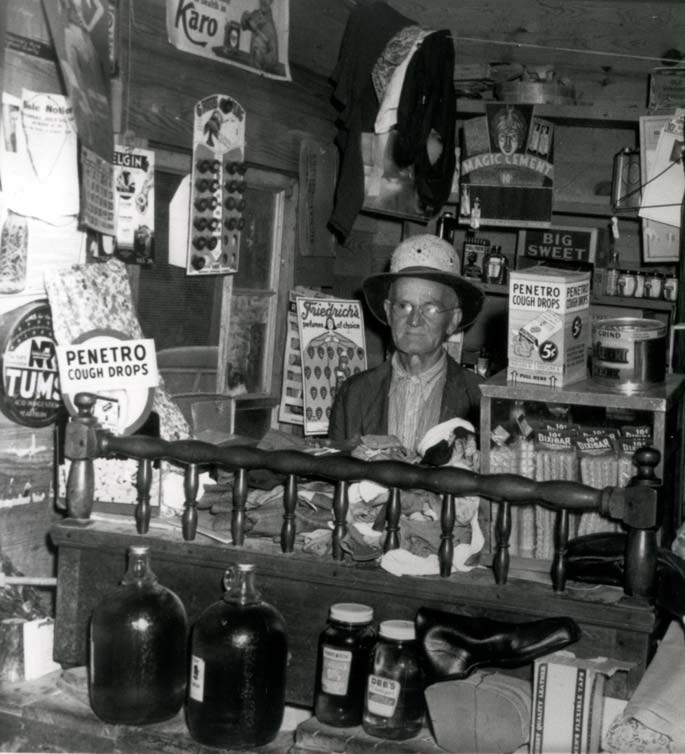 Circa 1918 photo of the inside of a general store in Gatlinburg, TN. Store owner behind counter with articles for sale surrounding him on counters and walls.