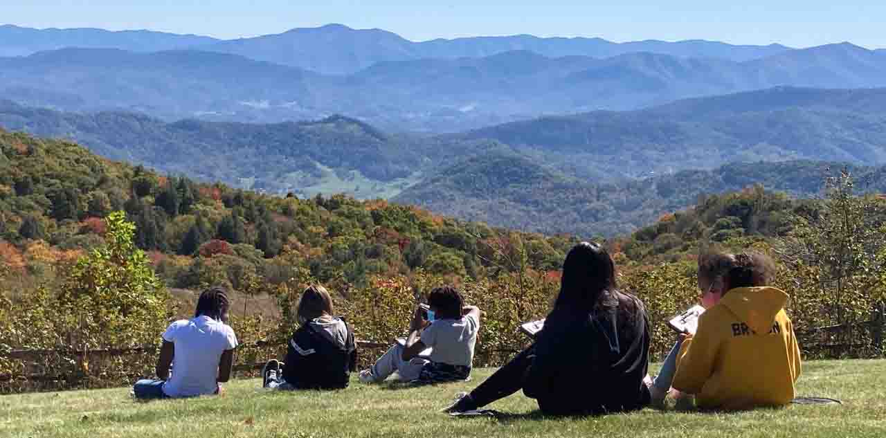 Students sitting on hill looking into the distance with mountains in the background.