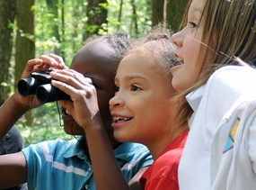 Three young girls use a pair of binoculars to explore the park. Three young girls use a pair of binoculars to explore the park.