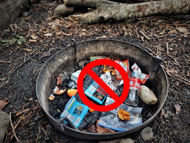 Garbage in fire pit Fire ring with pieces of trash in it. A red slash across it.
