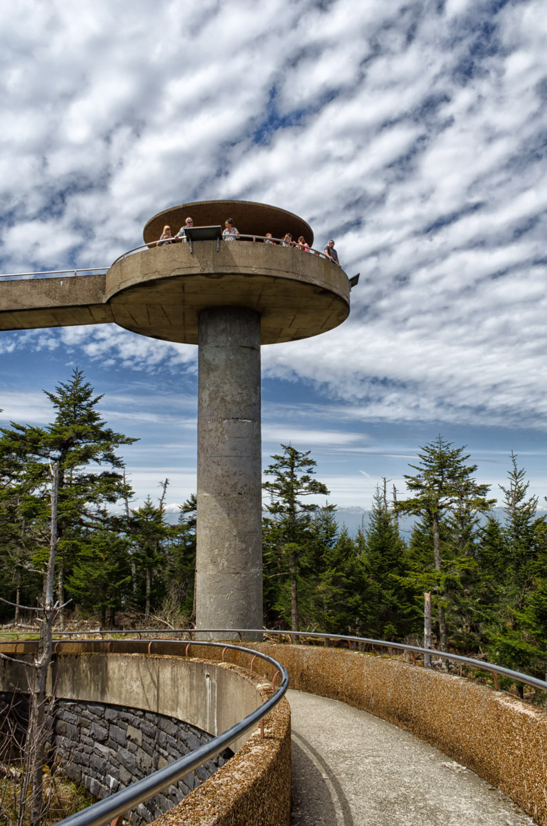 The photo shows a circular observation tower on a sunny day with a large, rounded walkway and white clouds in the sky.