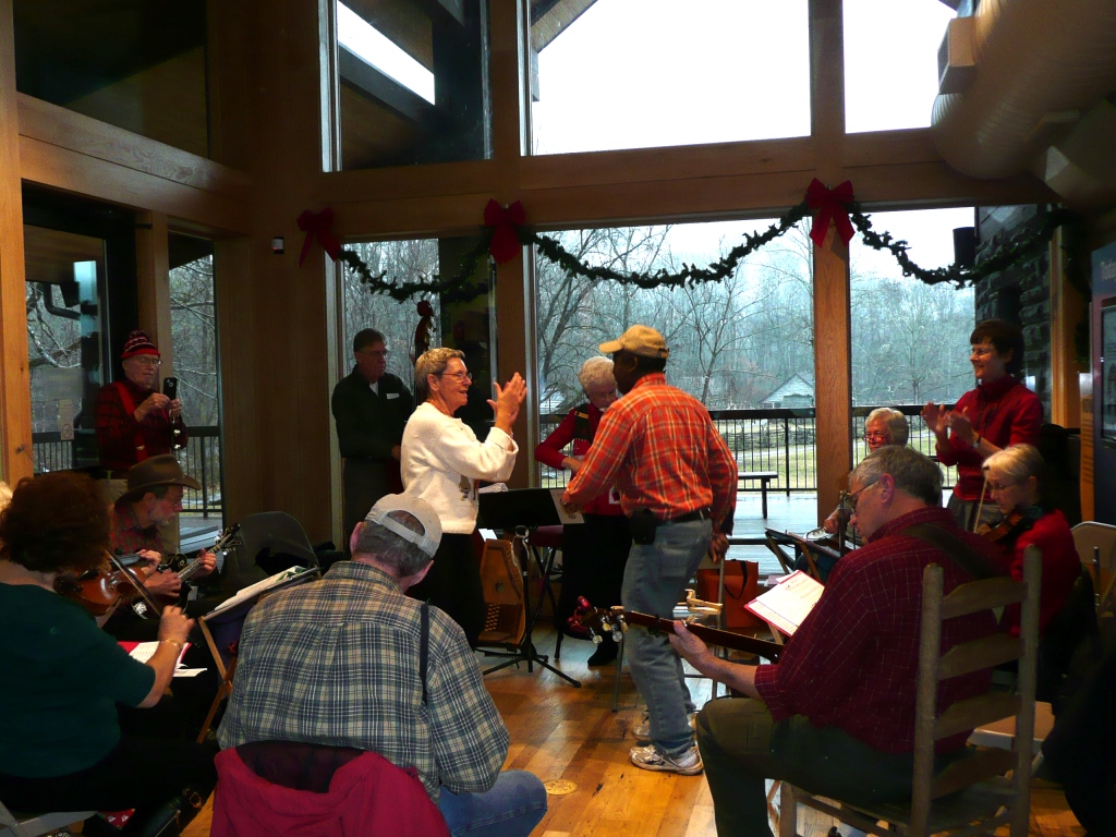 OVC Holiday Homecoming Two people clapping and dancing while surrounded by musicians in a building with large windows.