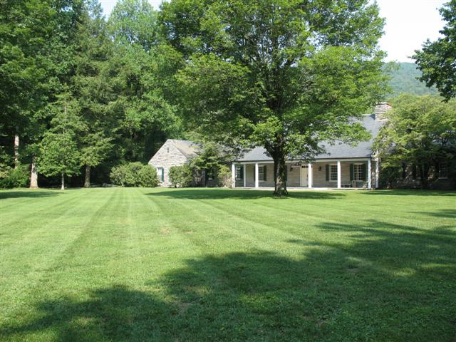 A stone building with a covered porch and a wide grassy lawn with multiple trees.