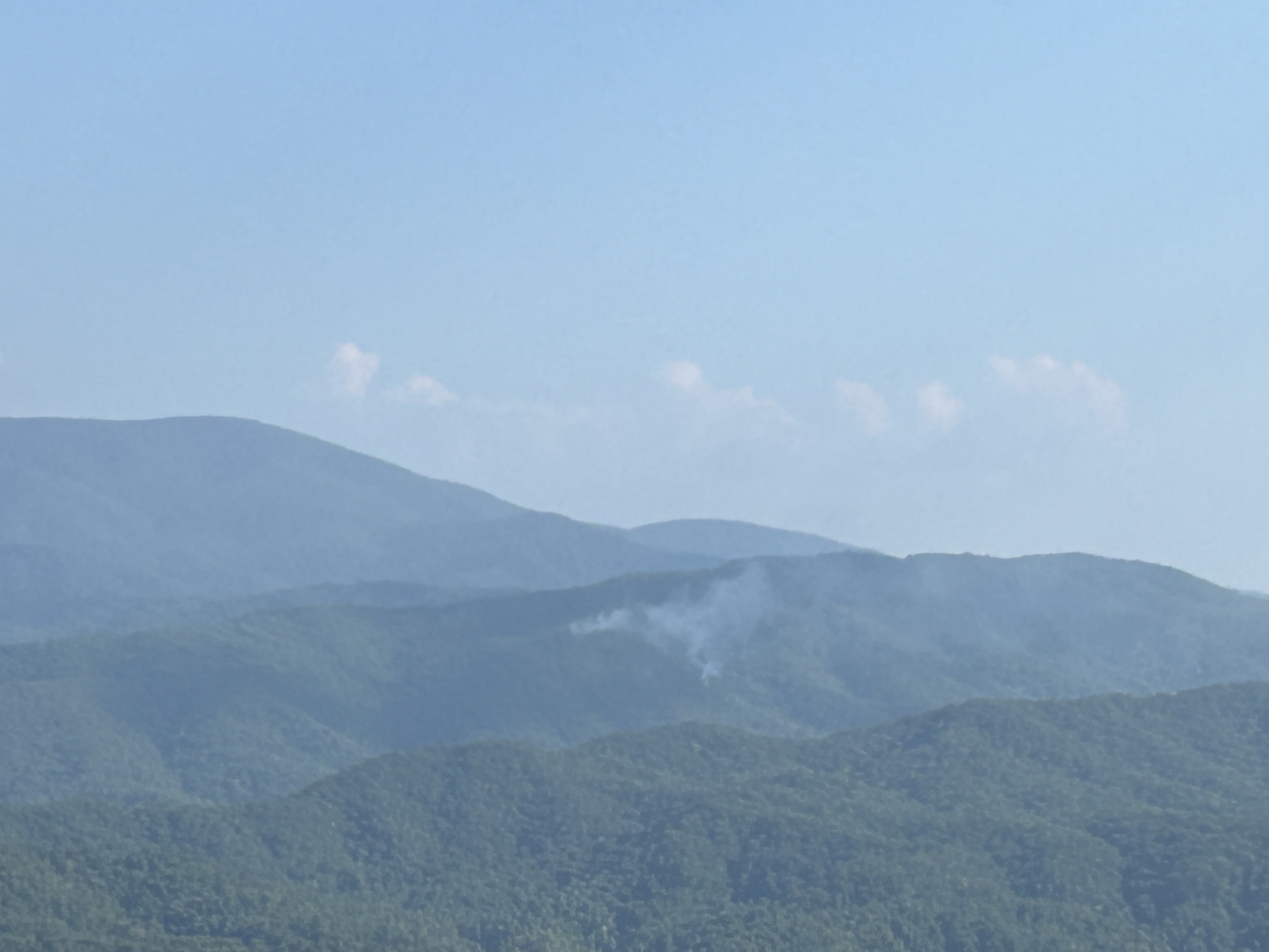 2024_08_29_fire update_NPS Photo A small plume of smoke rising from between rolling mountain ridges on a mostly clear day.