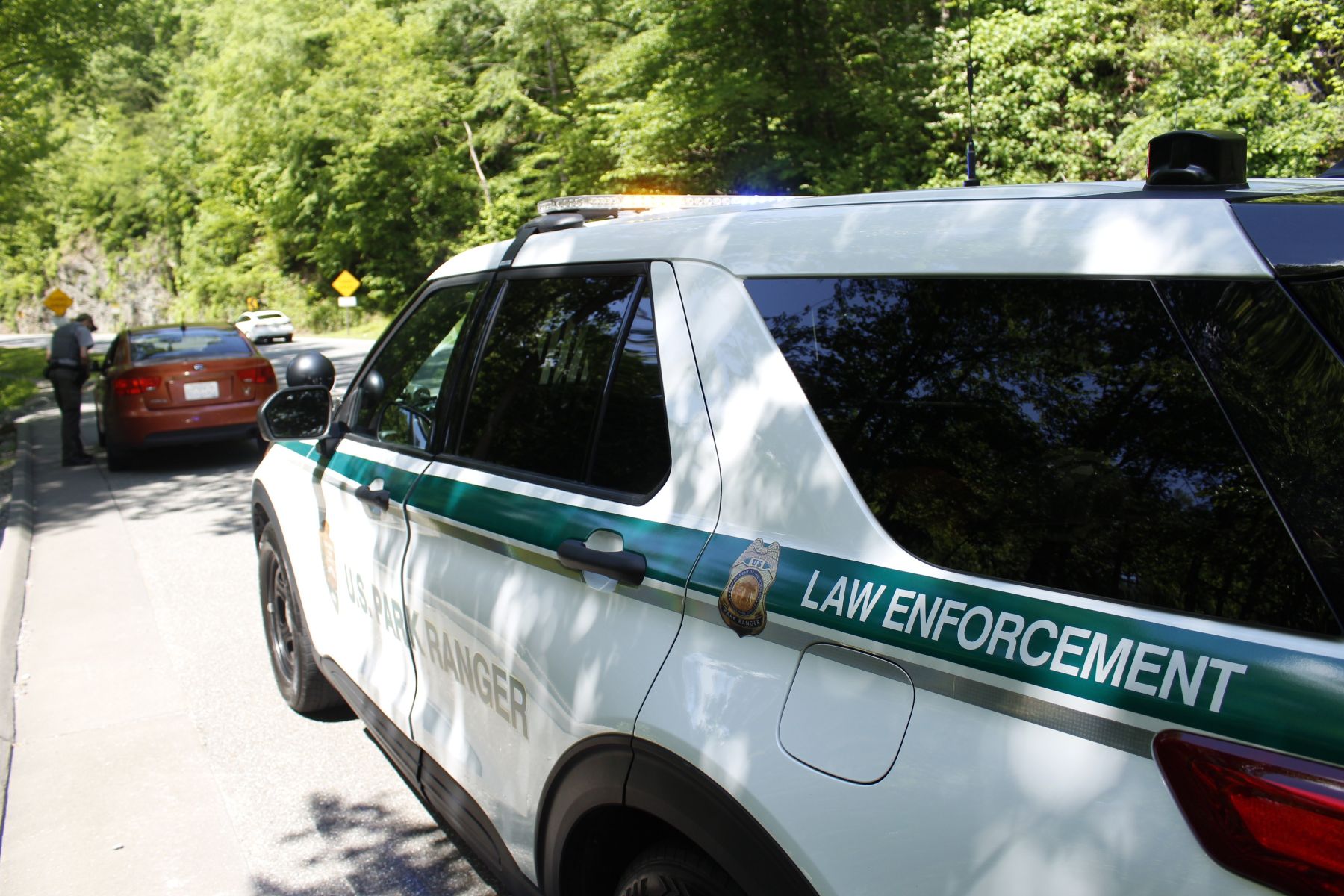 A park ranger law enforcement SUV at a roadside pull-off with an orange car pulled over. There is a law enforcement ranger next to the orange car.
