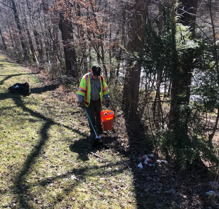 NPS Employee Picking Up Litter on the Spur 2021 Uniformed man in a safety vest picking up roadside trash in the forest.