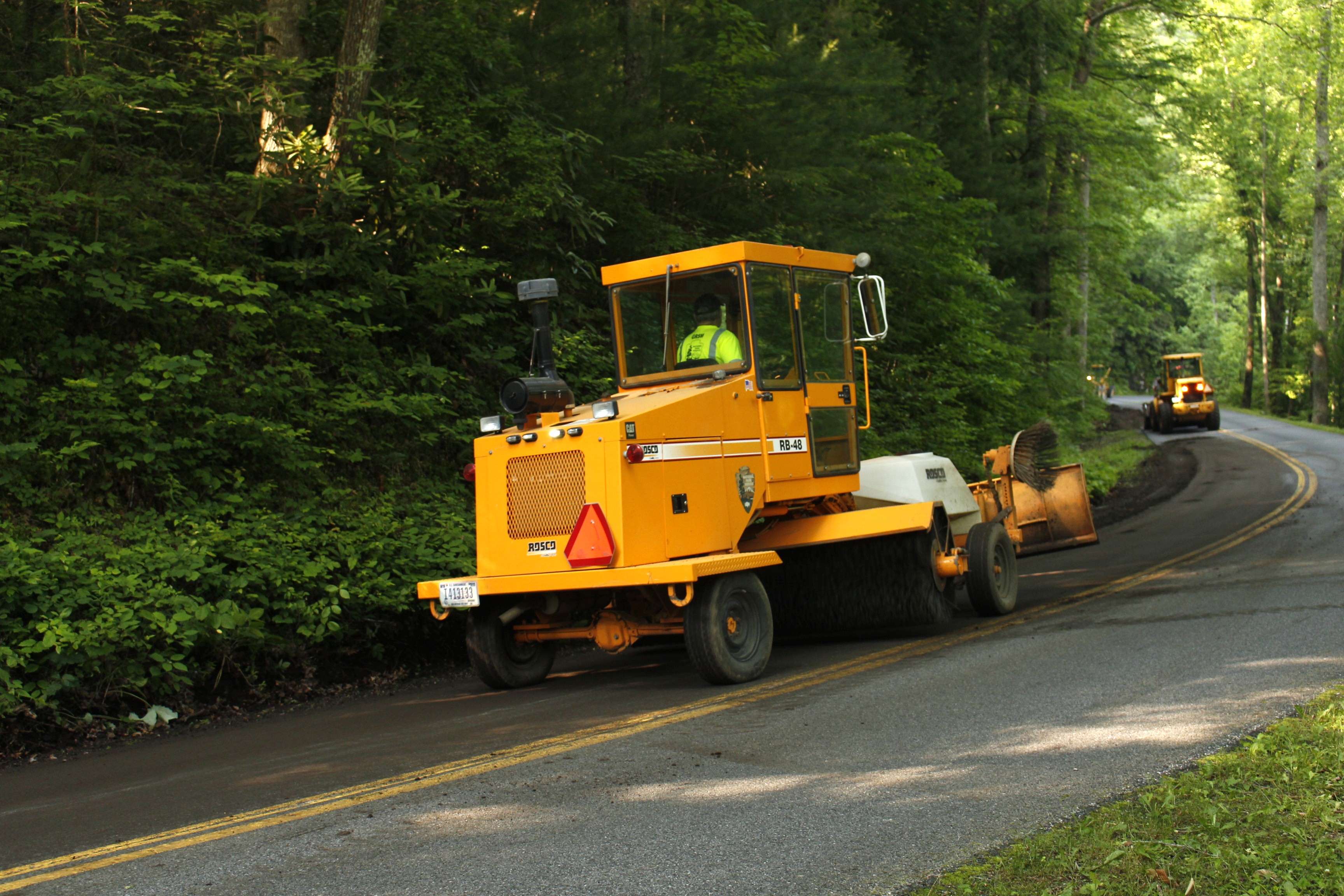 Construction vehicles clean dirt and debris from a forest road.