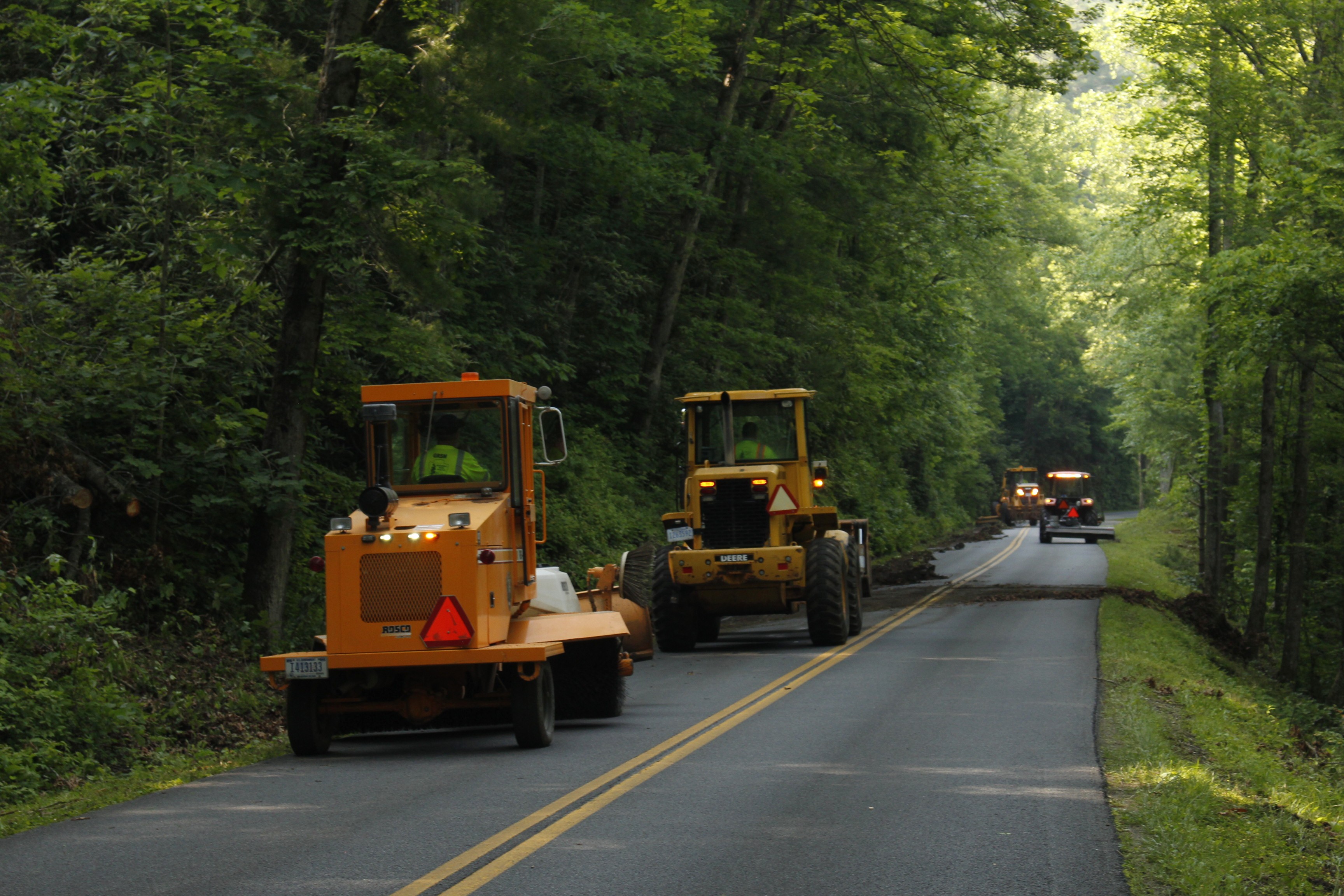 Three construction vehicles move down a mountain road as they complete mowing and cleanup.